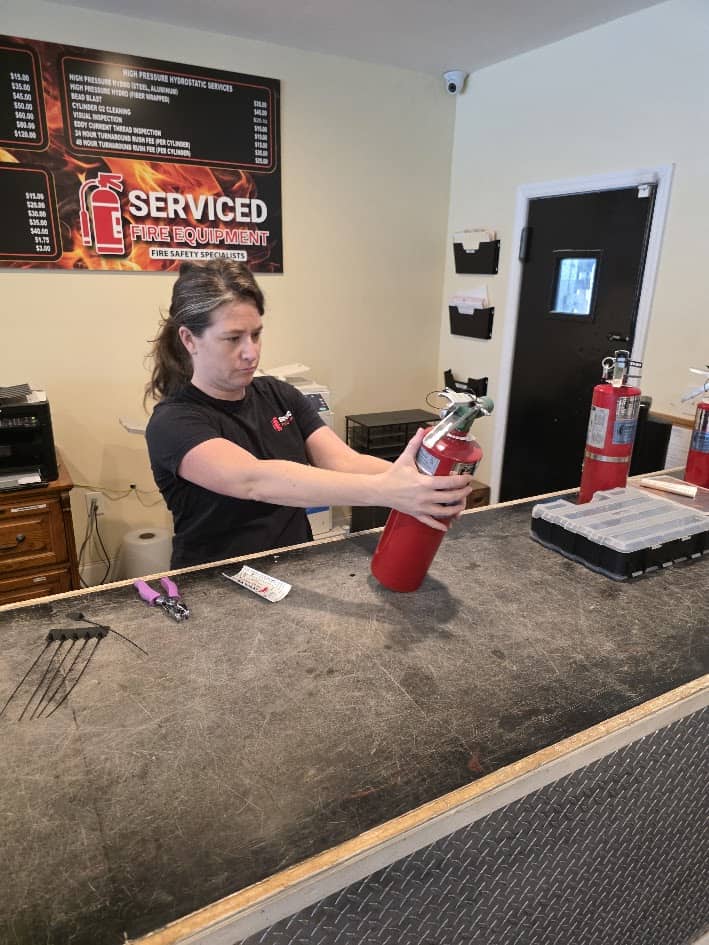 Technician inspecting a fire extinguisher gauge and condition at Serviced Fire Equipment
