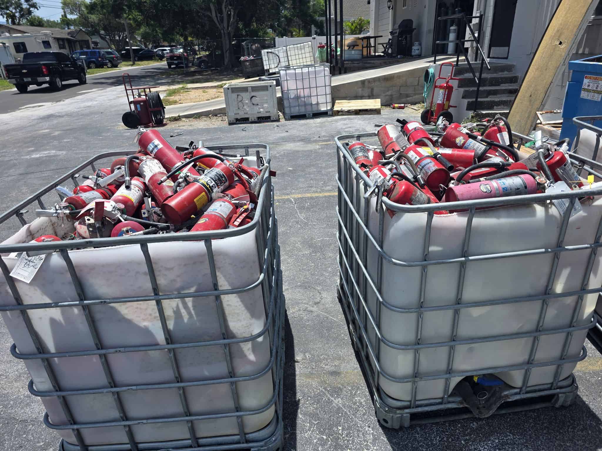 A variety of fire extinguisher types and brands accumulated for disposal — including ABC dry chemical, CO₂, wet chemical Class K, and pre-engineered system cylinders